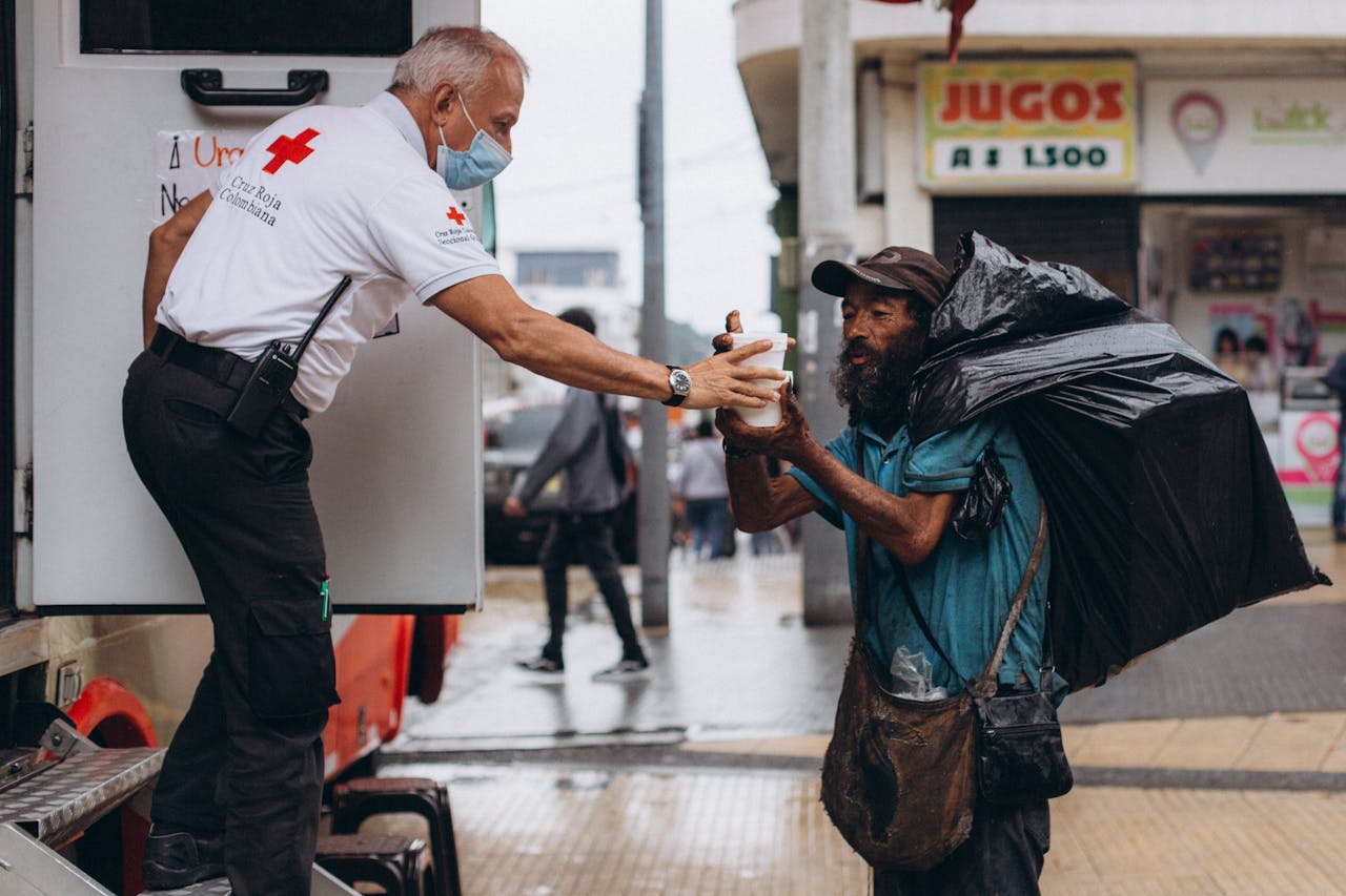 Red Cross worker assisting a homeless man outdoors with kindness.