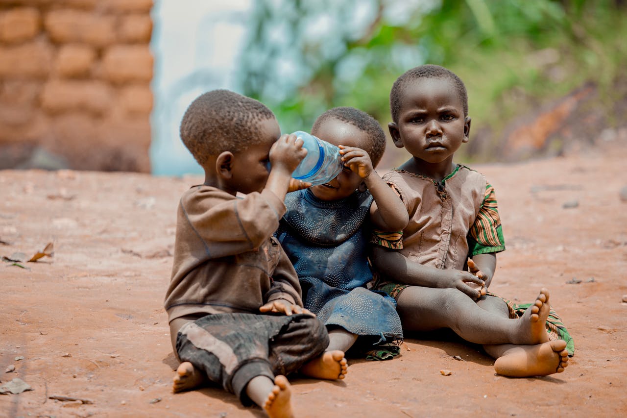 Children sitting outdoors on a dirt path, sharing a moment. Captured in a natural setting.